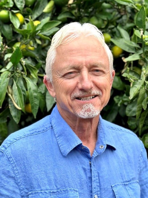 A man with white hair and blue shirt smiling.